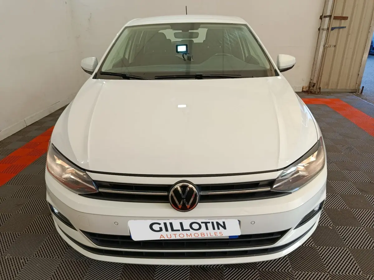 Vue avant d'une Volkswagen Polo blanche 2020, avec calandre noire et phares allumés dans un garage.