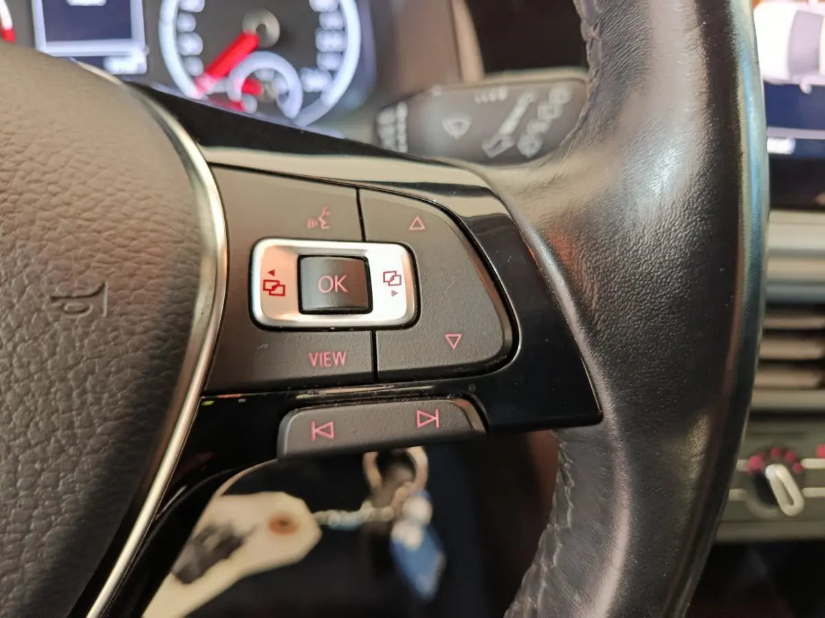 Gros plan sur les commandes gauche du volant cuir noir d'une Volkswagen Polo blanche, tableau de bord en arrière-plan flou.