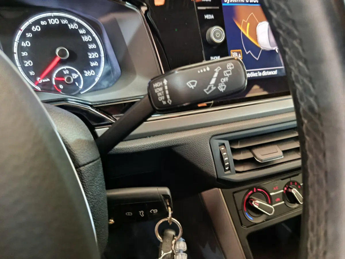 Gros plan sur le tableau de bord et volant de la Volkswagen Polo blanche 2020, avec écran tactile et commandes visibles.