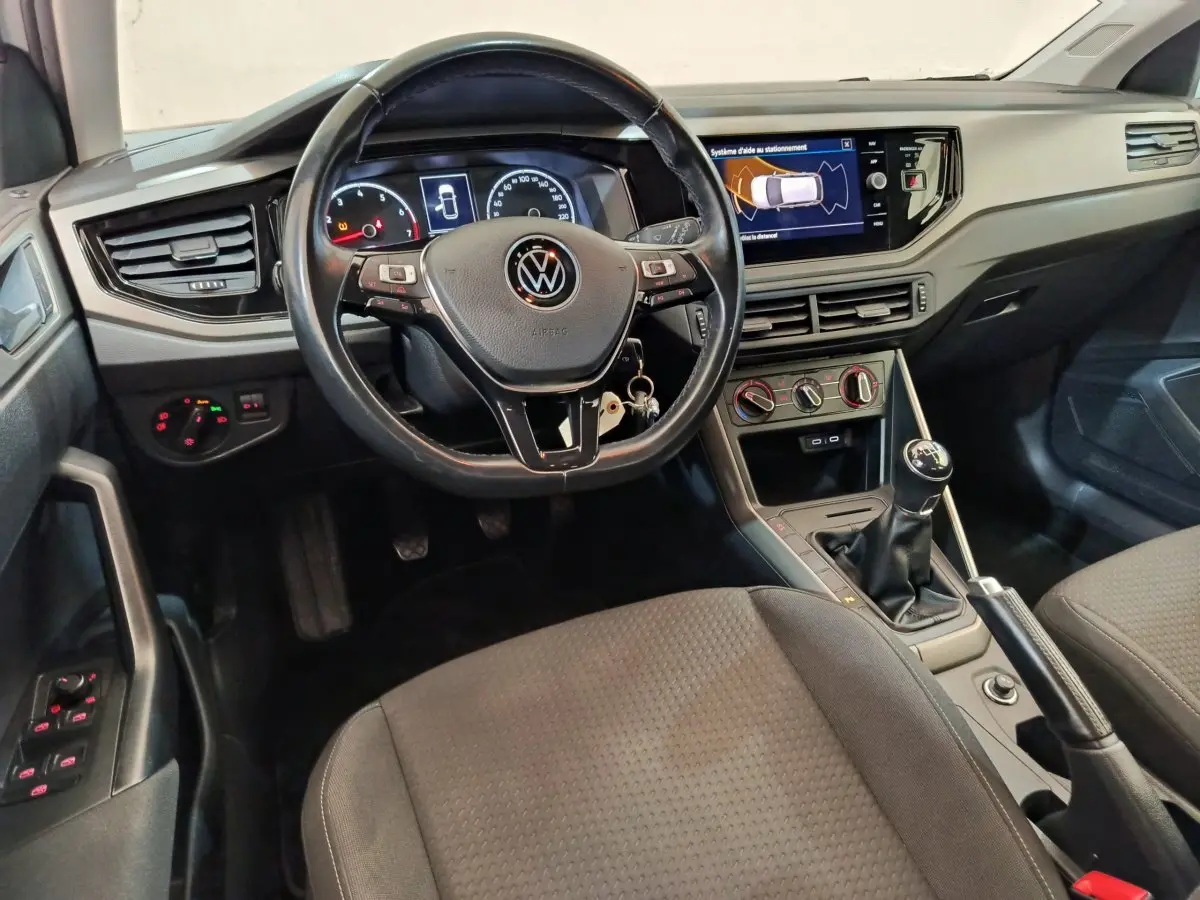 Vue intérieure avant de la Volkswagen Polo 1.0 TSI 95 Lounge Business, tableau de bord noir avec écran tactile et volant cuir.