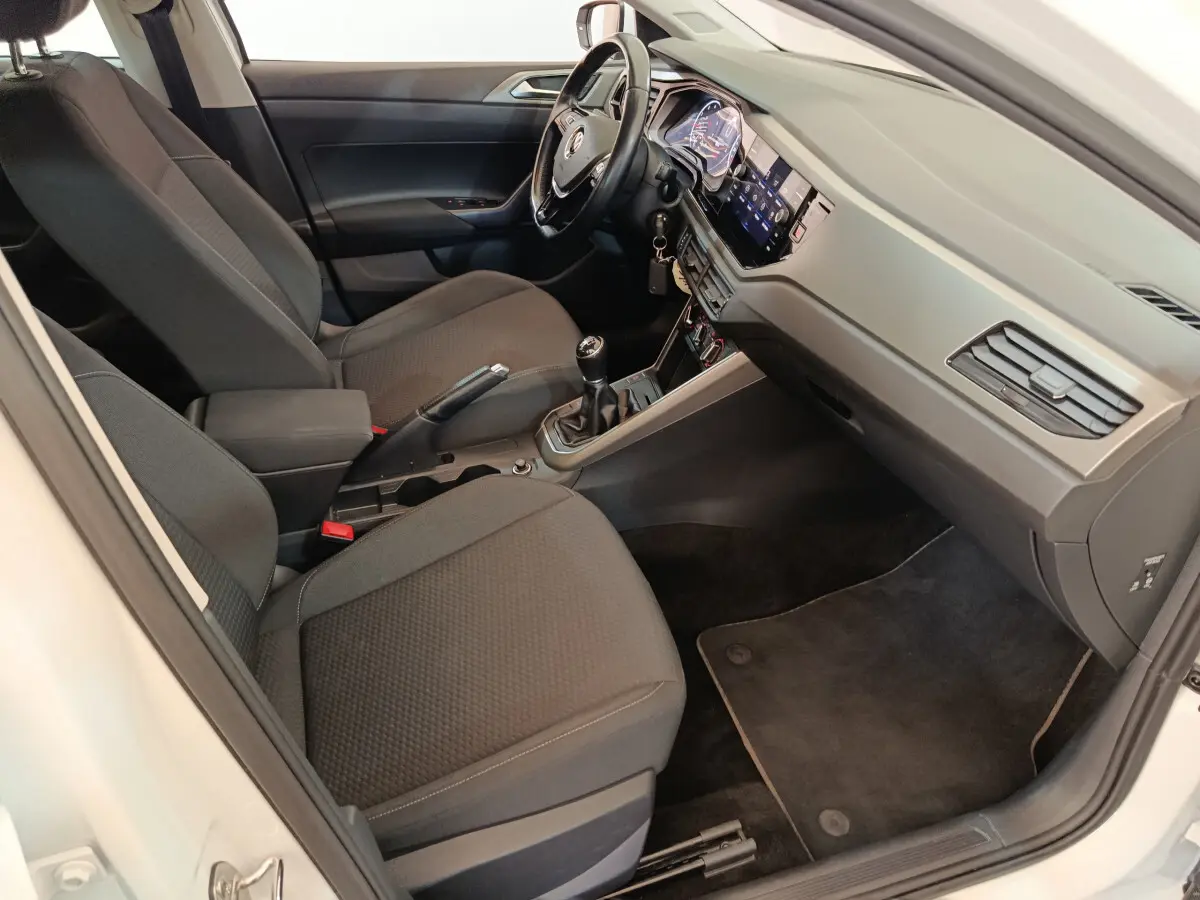 Intérieur de la Volkswagen Polo blanche 2020, vue côté conducteur, tableau de bord moderne avec écran tactile et volant cuir.