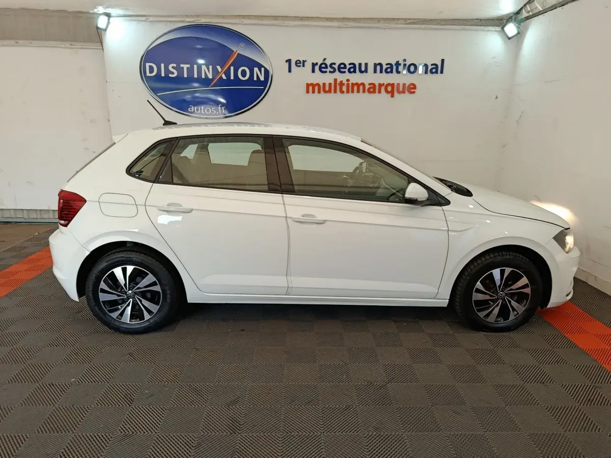 Profil droit d'une Volkswagen Polo blanche 2020 avec jantes alliage et feux avant allumés en intérieur showroom