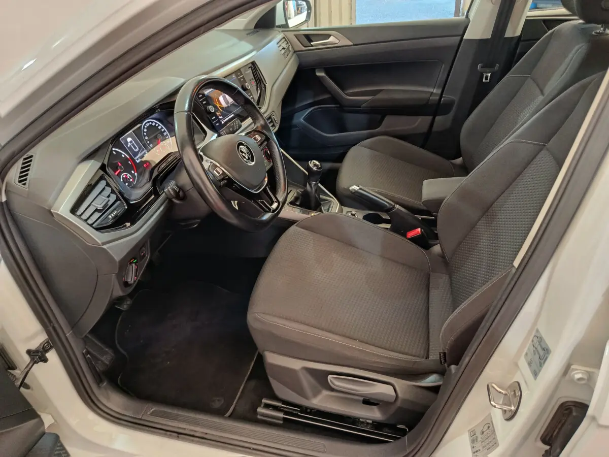Intérieur avant droit de la Volkswagen Polo blanche 2020, montrant sièges tissu gris et tableau de bord avec écran tactile.