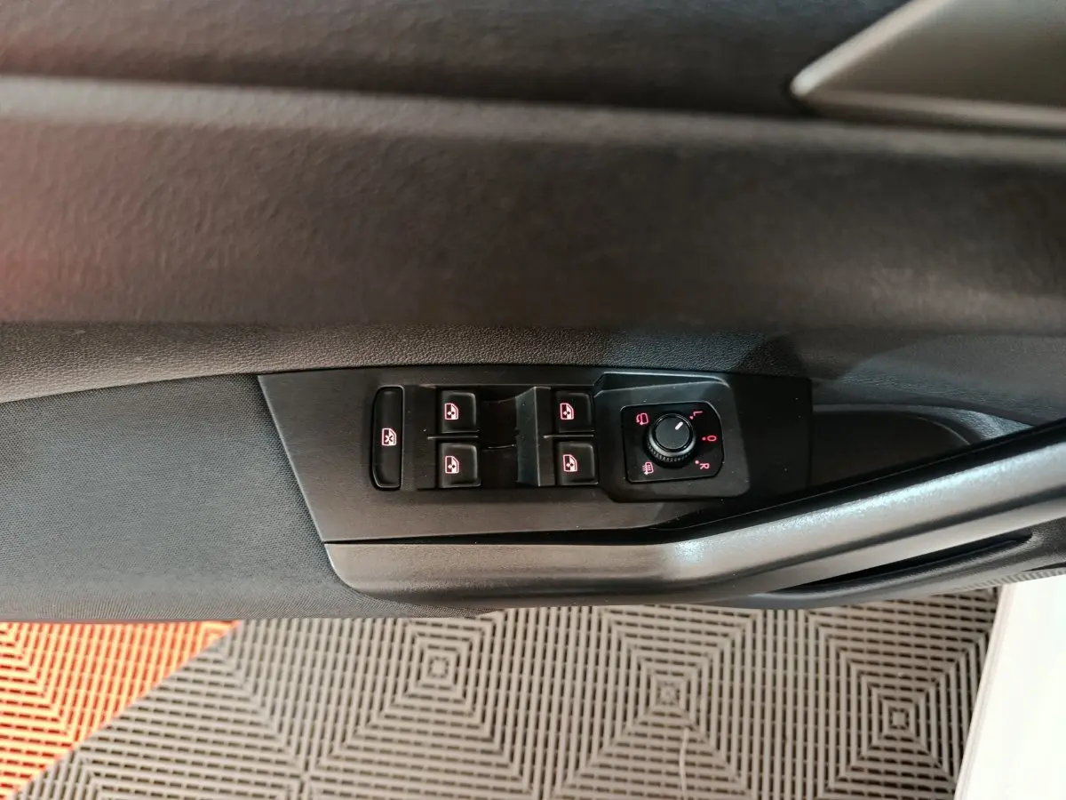 Gros plan sur les commandes de lève-vitres et rétroviseurs sur la porte côté conducteur d'une Volkswagen Polo blanche.