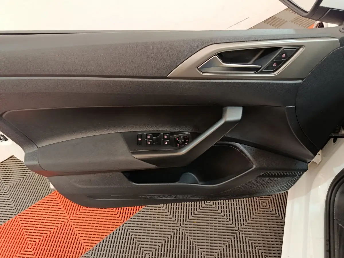 Vue rapprochée de la porte côté conducteur noire d'une Volkswagen Polo blanche, avec commandes électriques intégrées.