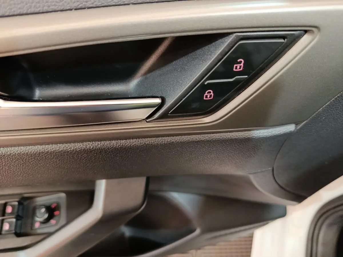 Poignée intérieure côté conducteur de Volkswagen Polo blanche, avec boutons de verrouillage éclairés en rouge.