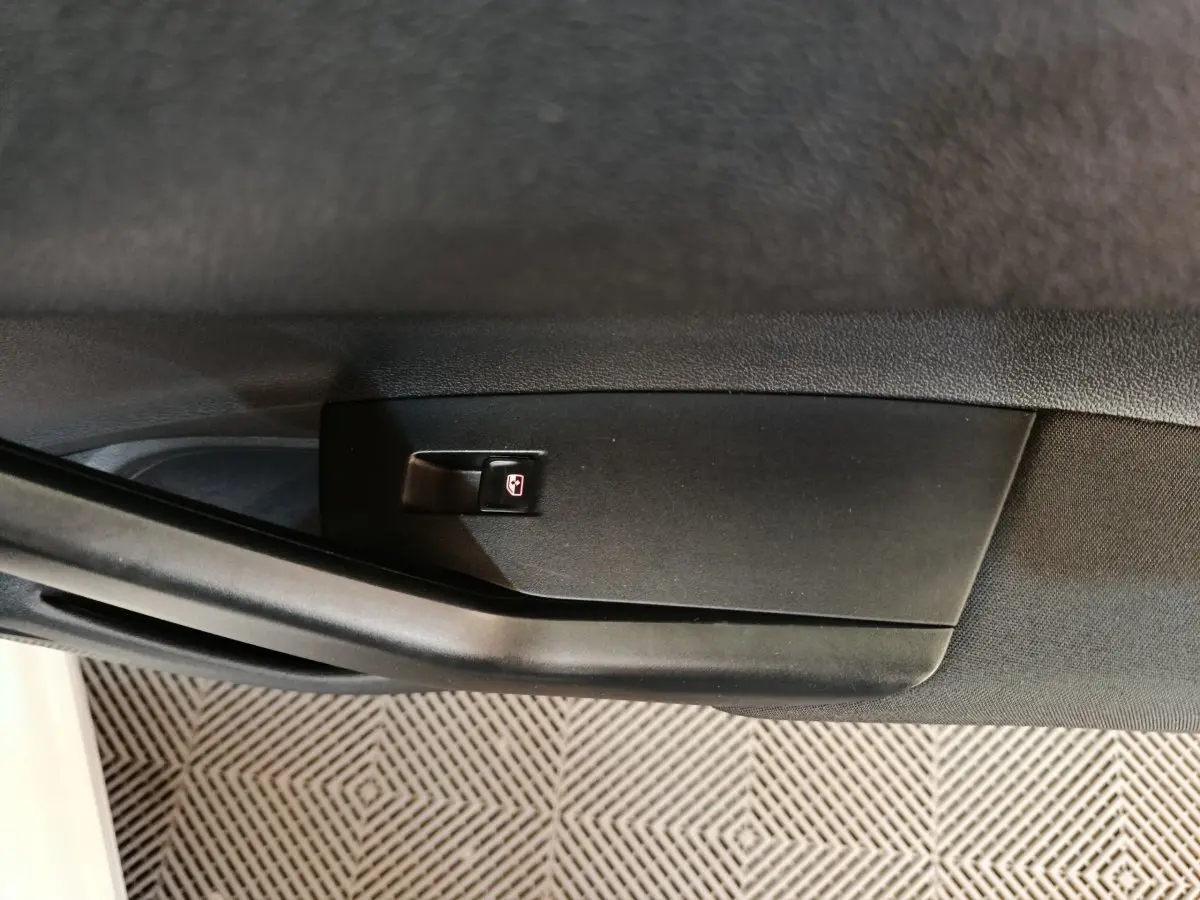 Gros plan sur le bouton de verrouillage des vitres sur la porte intérieure côté gauche d'une Volkswagen Polo blanche.