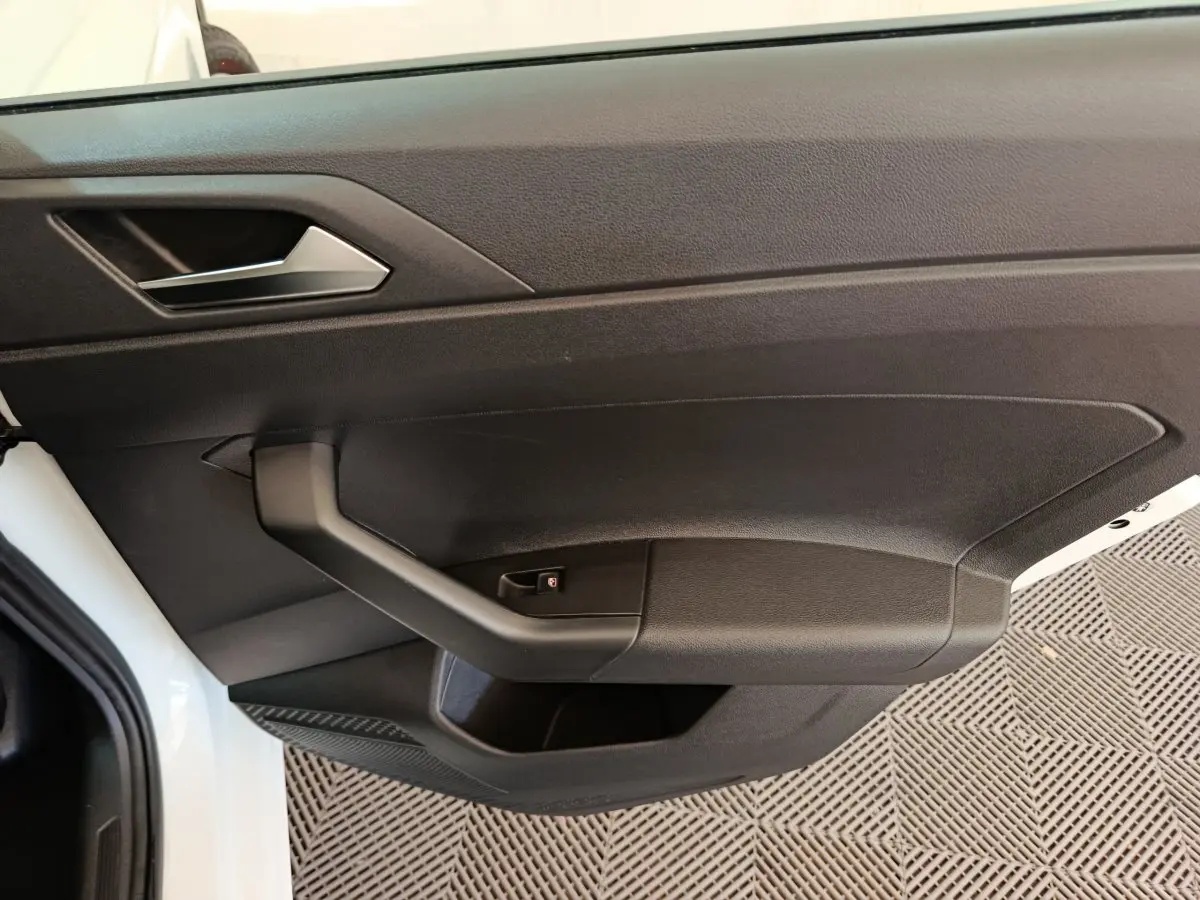 Vue rapprochée de la porte avant gauche noire d'une Volkswagen Polo blanche avec poignée intégrée et bouton de verrouillage.