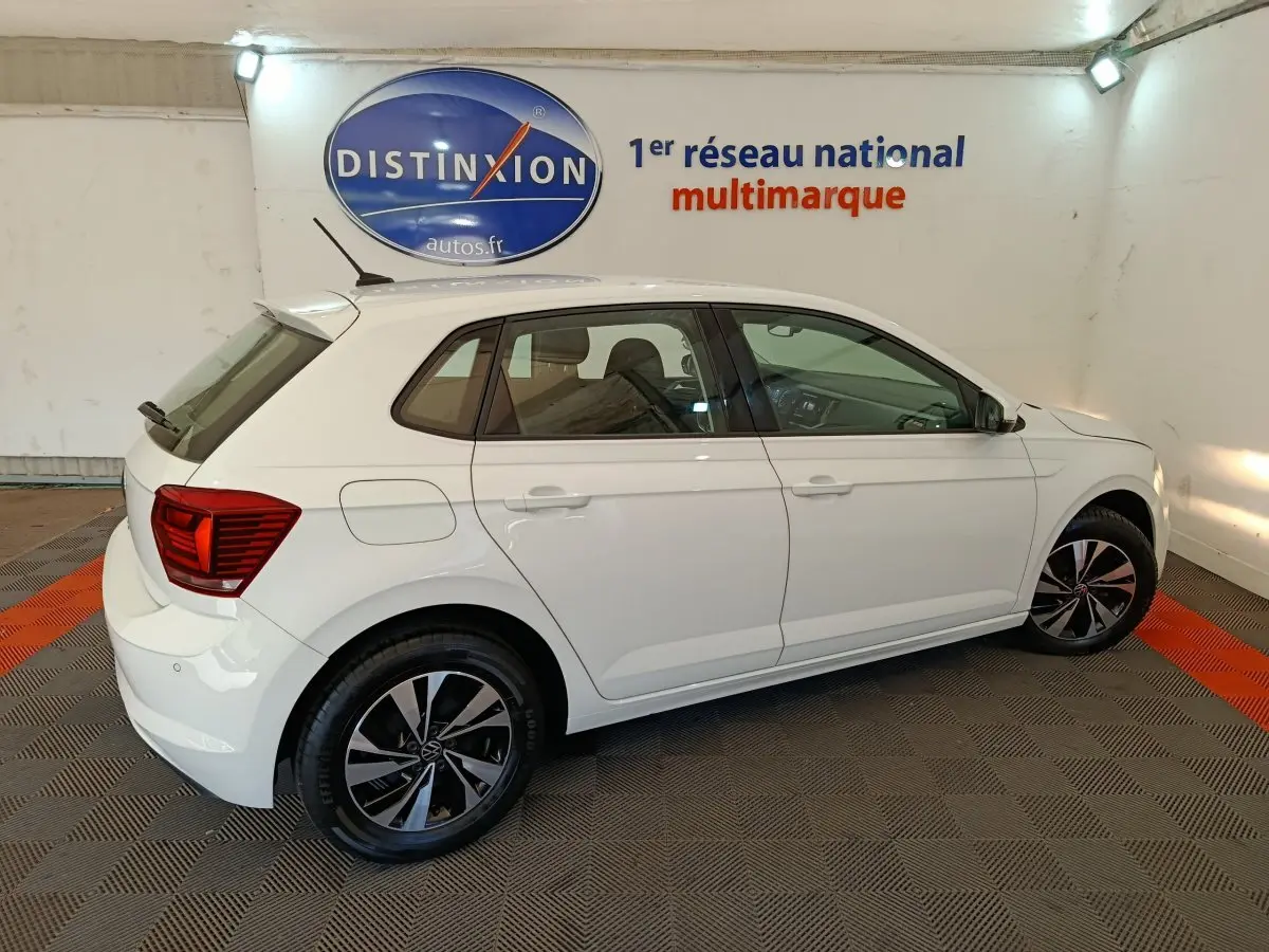 Volkswagen Polo blanche vue de profil côté gauche dans un showroom avec jantes alliage et feux arrière rouges.