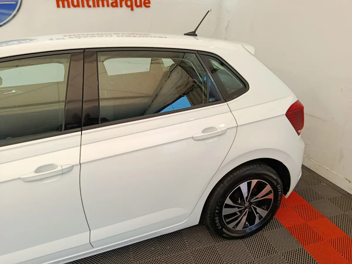 Vue latérale droite d'une Volkswagen Polo blanche 2020 avec jantes alliage et vitres teintées en intérieur showroom.