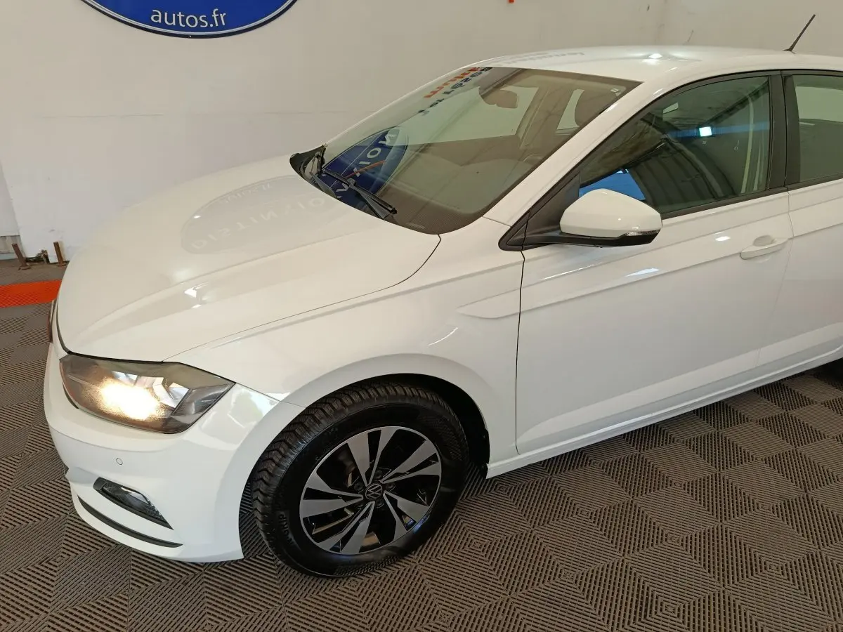 Vue 3/4 avant droit d'une Volkswagen Polo blanche avec phares allumés et jantes alliage noires.