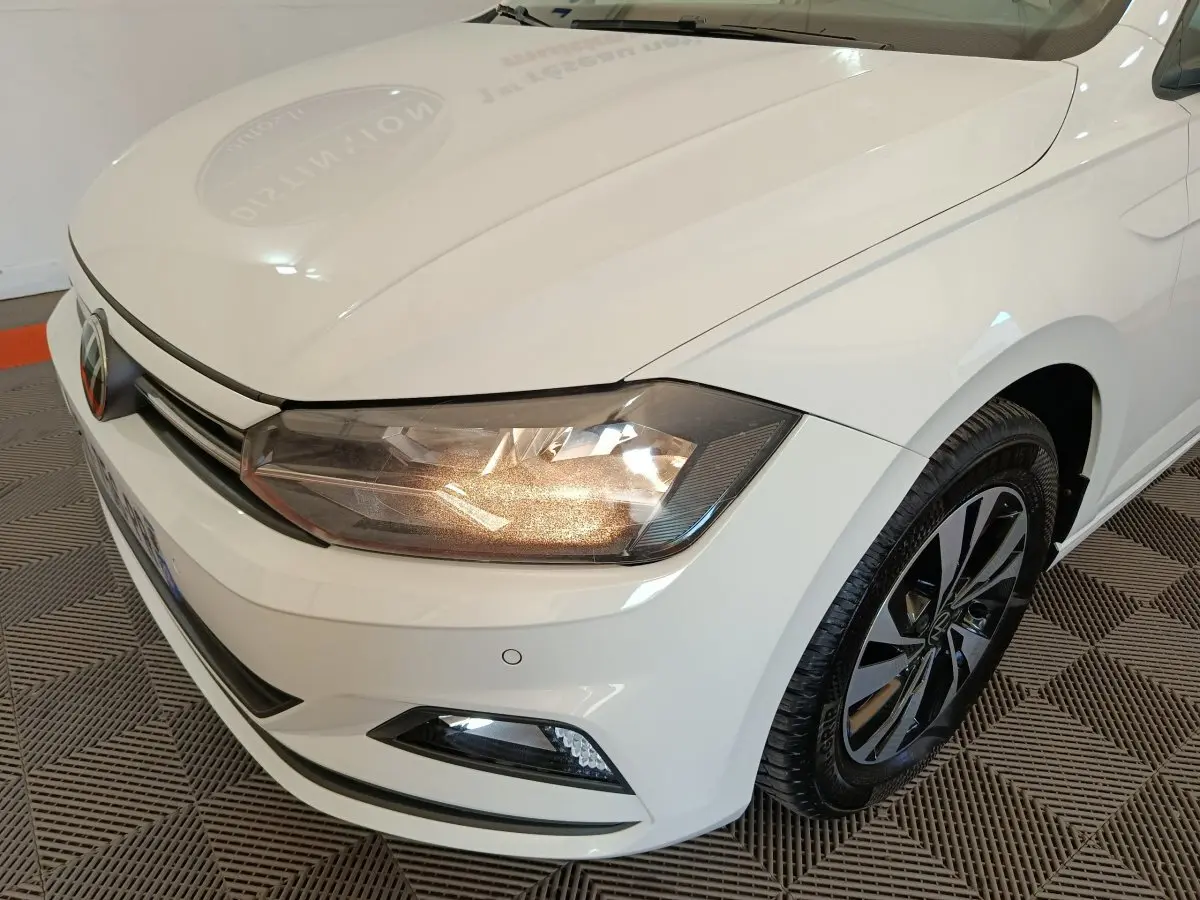 Vue 3/4 avant droit d'une Volkswagen Polo blanche avec phares allumés et jantes alliage noir et argent.