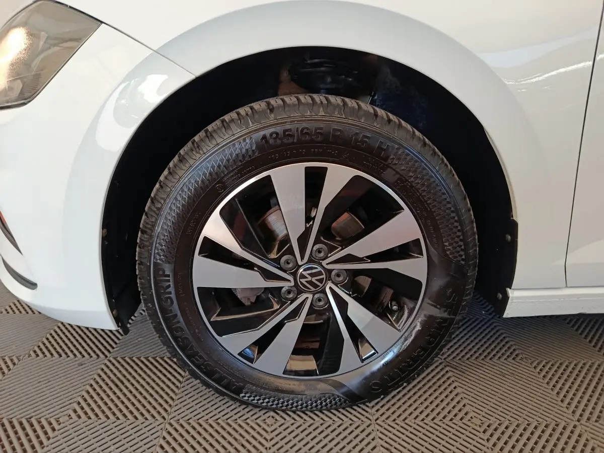 Gros plan sur la roue avant gauche d'une Volkswagen Polo blanche, avec jante alliage bicolore et logo VW central.