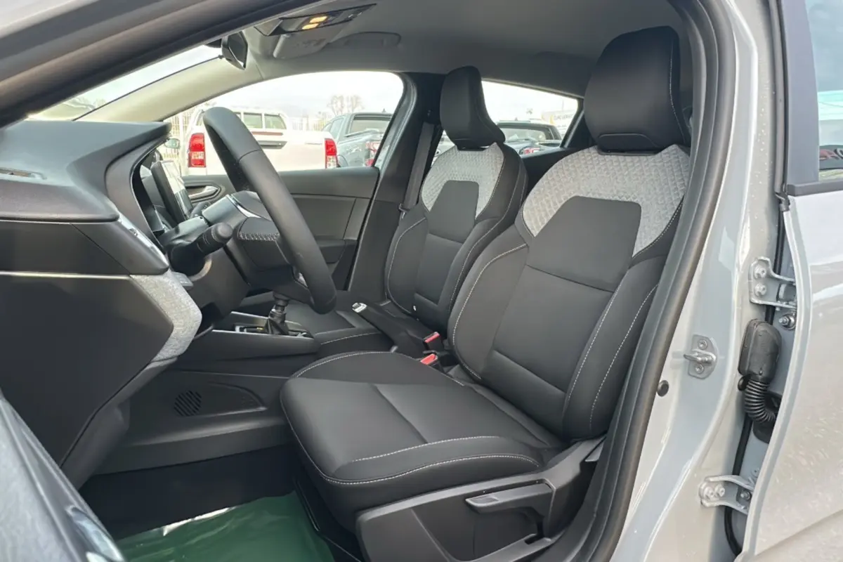 Vue intérieure côté conducteur de la Renault Clio gris rafale 2025, sièges avant en tissu noir avec inserts gris.