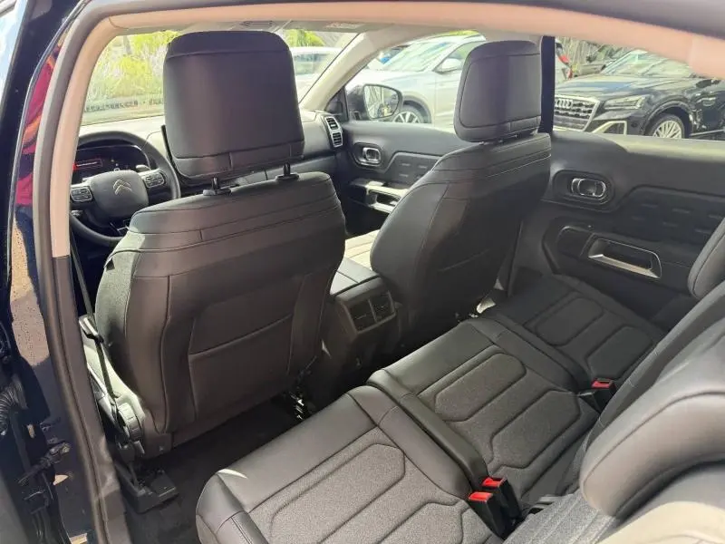 Vue intérieure arrière du Citroën C5 Aircross 2025, sièges noirs en cuir et tissu, avec console centrale et aérateurs visibles.