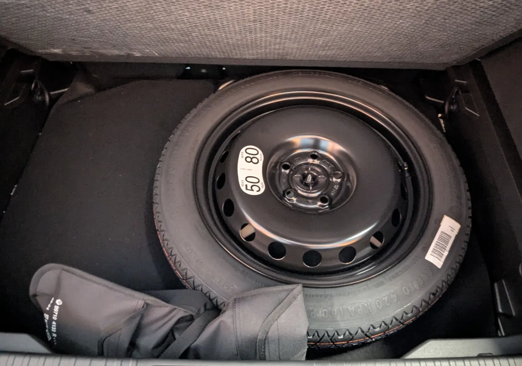 Roue de secours compacte noire dans le coffre d'un Renault Captur E-Tech hybride 2025, avec housse de protection partielle.