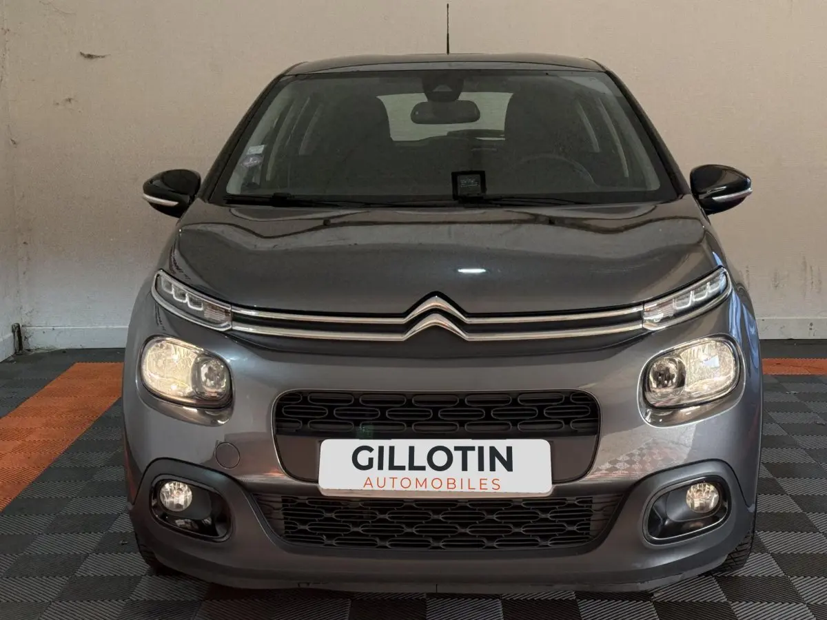 Vue frontale d'une Citroën C3 gris clair, avec phares allumés et calandre noire distinctive.