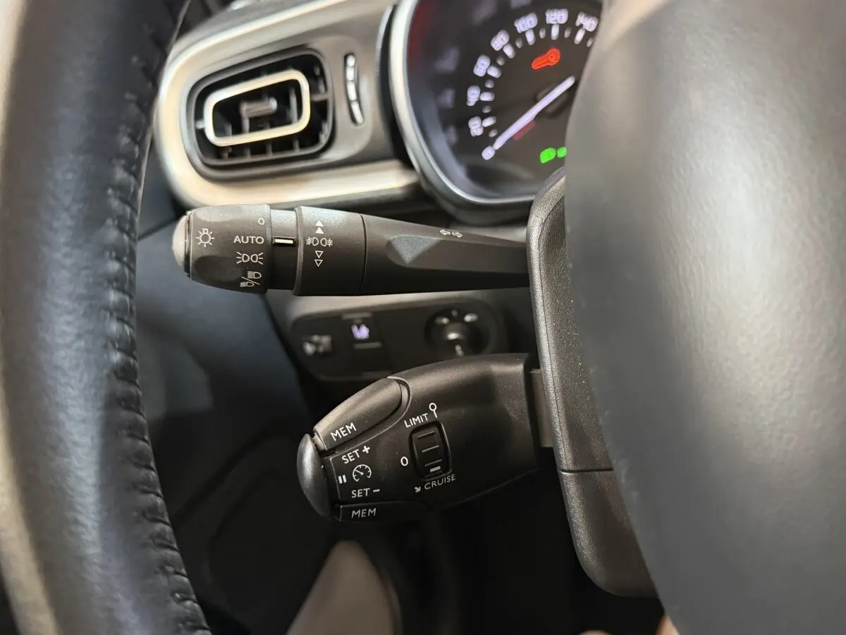 Gros plan sur les commandes au volant noir et tableau de bord éclairé d'une Citroën C3 gris clair, côté gauche.