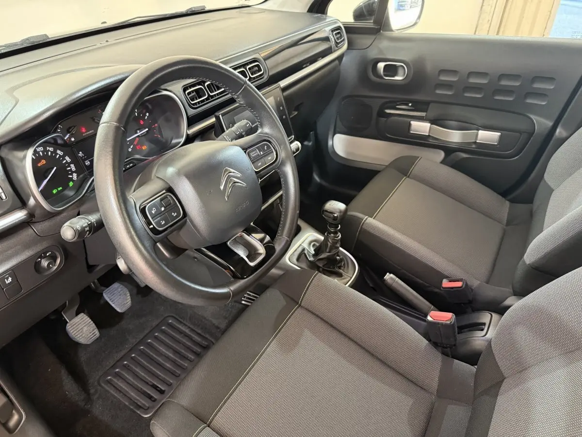 Vue intérieure côté conducteur de la Citroën C3 2019, tableau de bord noir avec volant cuir et sièges gris foncé.