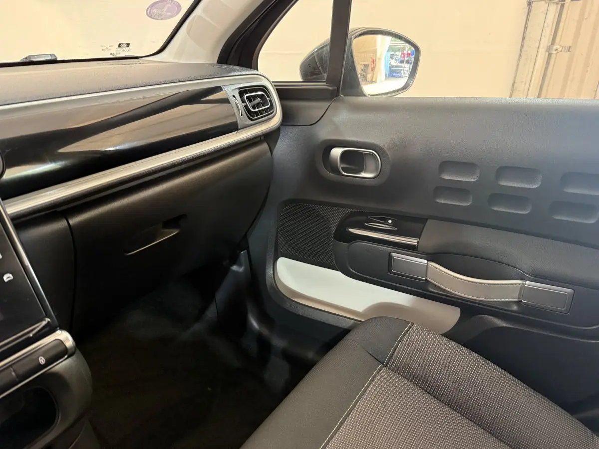 Intérieur côté passager de la Citroën C3 gris clair, montrant la porte avec poignée beige et tableau de bord noir.