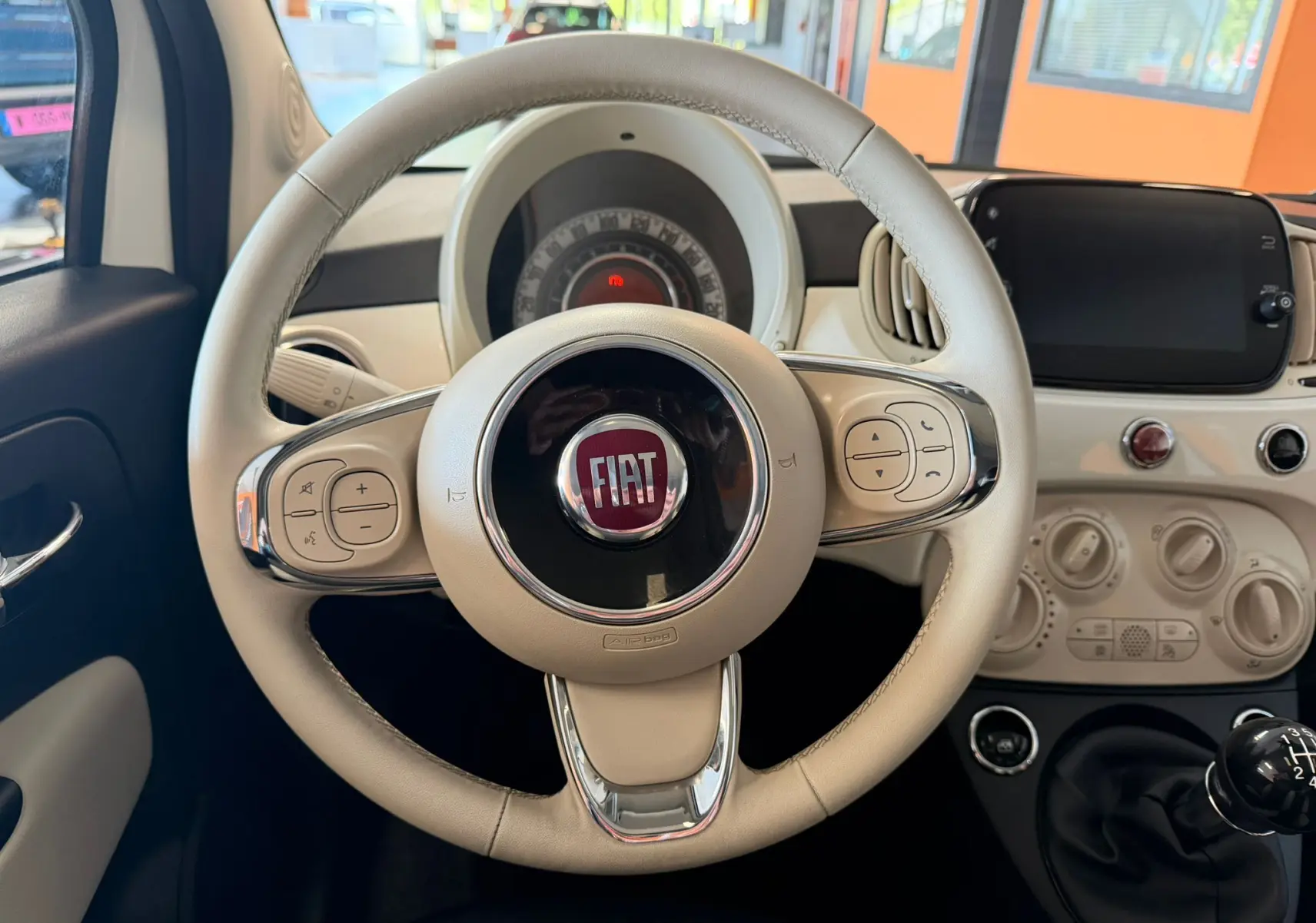 Vue rapprochée du volant beige clair de la Fiat 500 Dolcevita 2022 avec tableau de bord et levier de vitesses manuel.