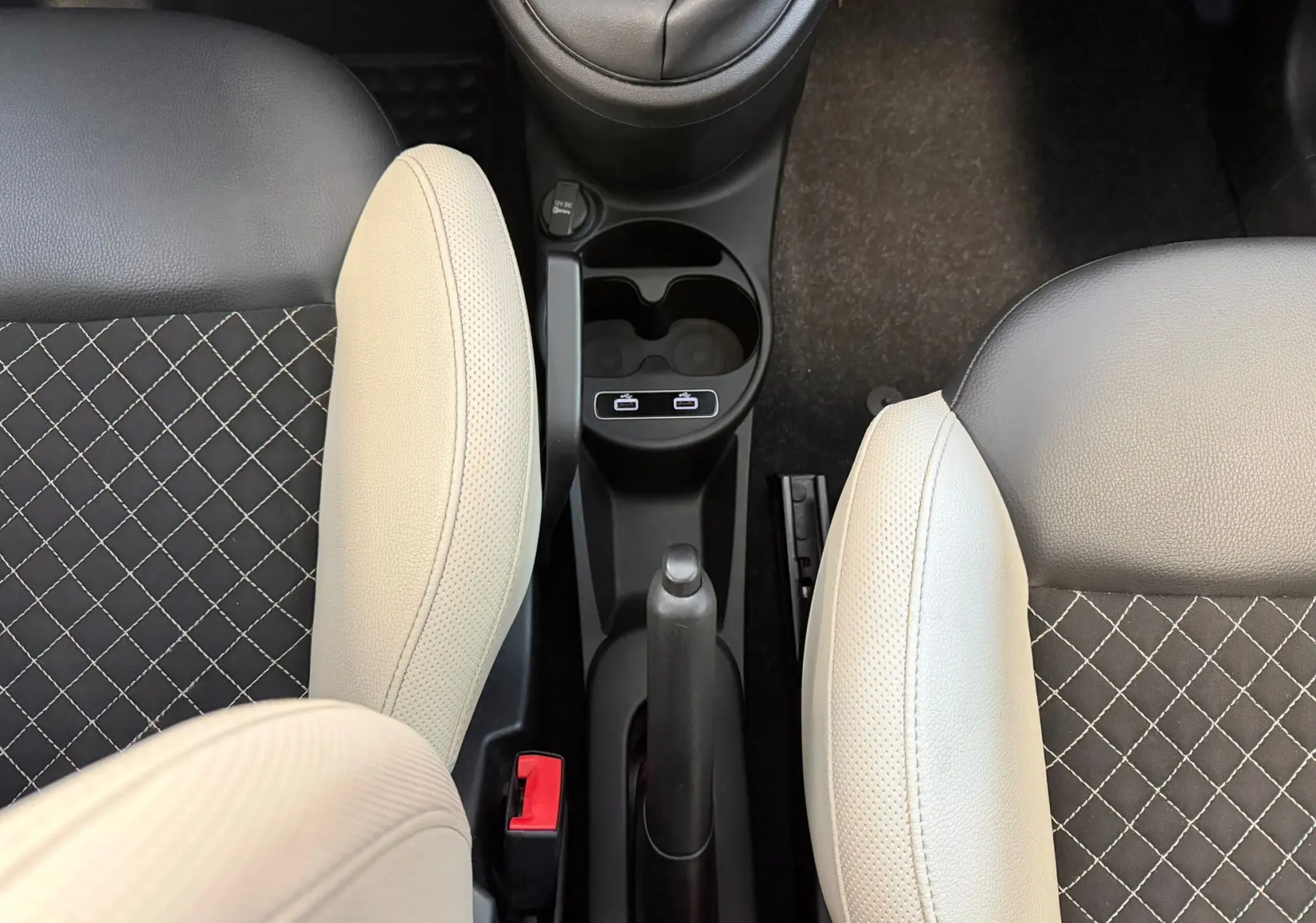 Vue plongeante sur la console centrale et les sièges avant bicolores beige et noir avec surpiqûres croisées du Fiat 500 2022.