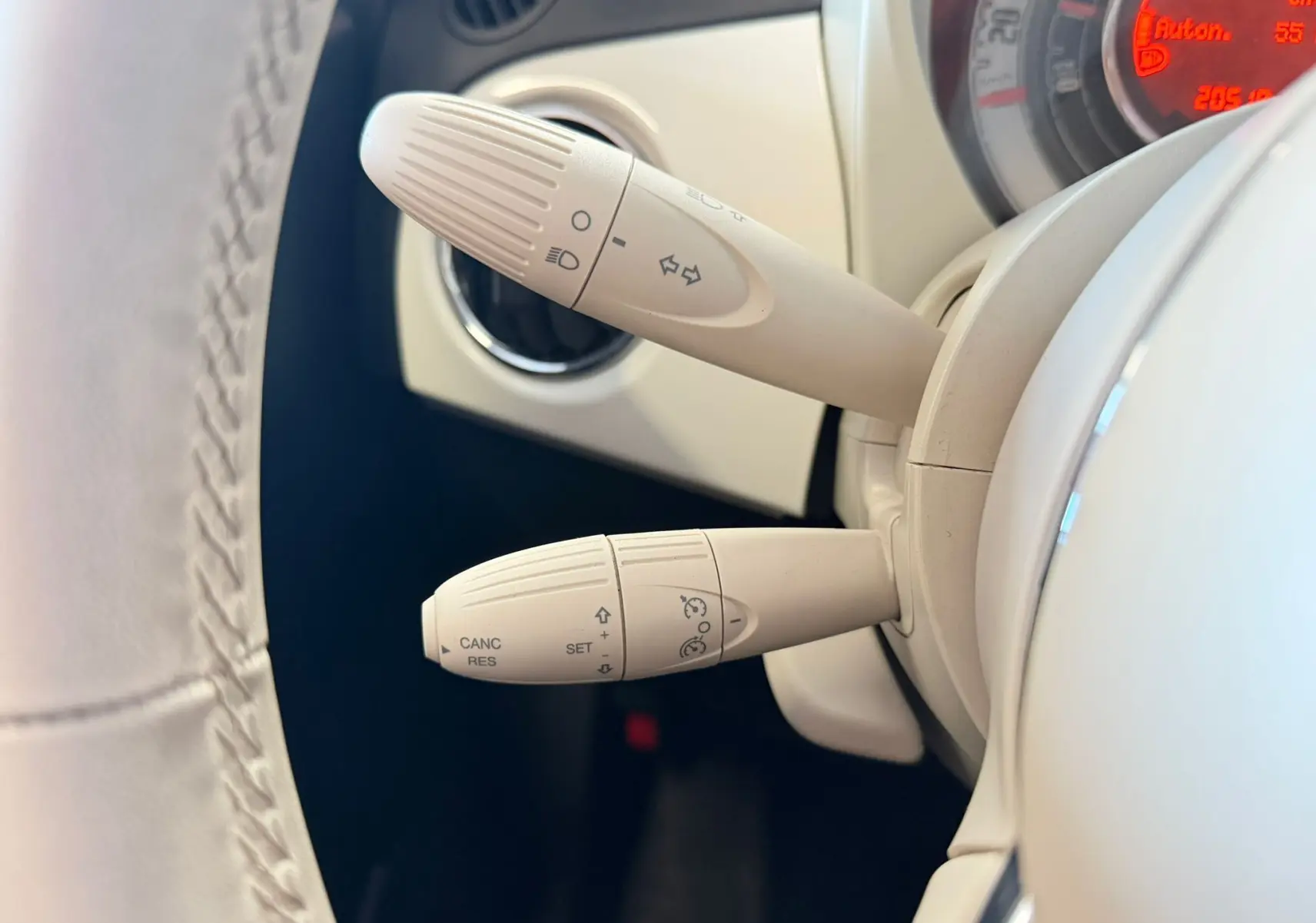 Gros plan sur les commandes de clignotants et régulateur de vitesse beiges du tableau de bord d'une Fiat 500 blanche.