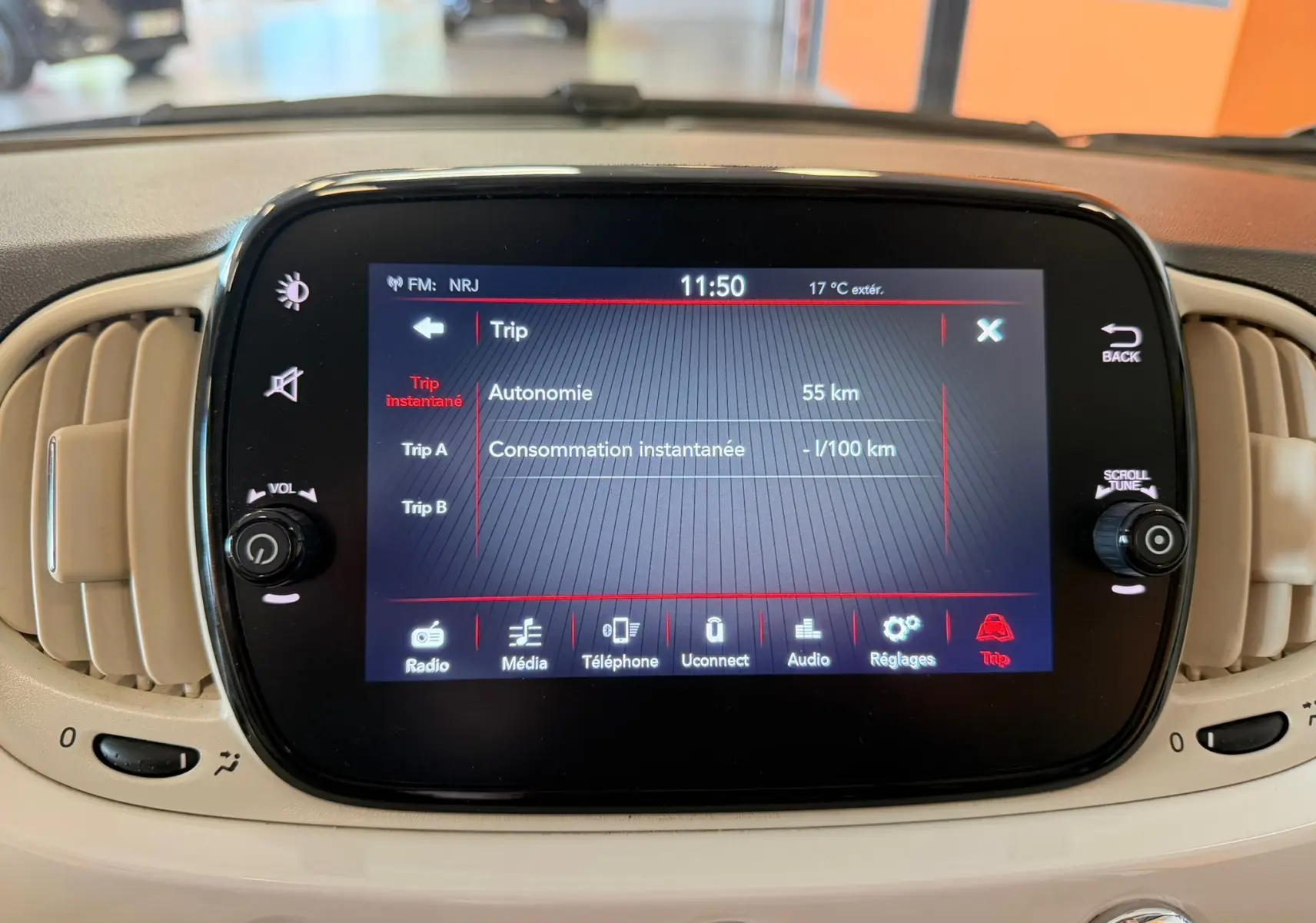 Écran tactile central de la Fiat 500 blanche en vue frontale, affichant les informations de trajet et réglages.