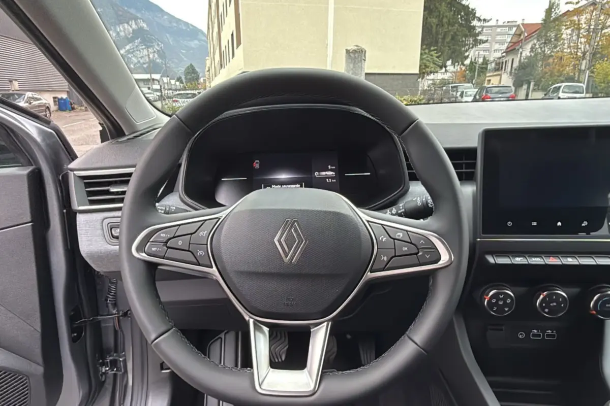 Vue intérieure centrée sur le volant cuir multifonctions d’une Renault Clio gris schiste avec tableau de bord et écran tactile.