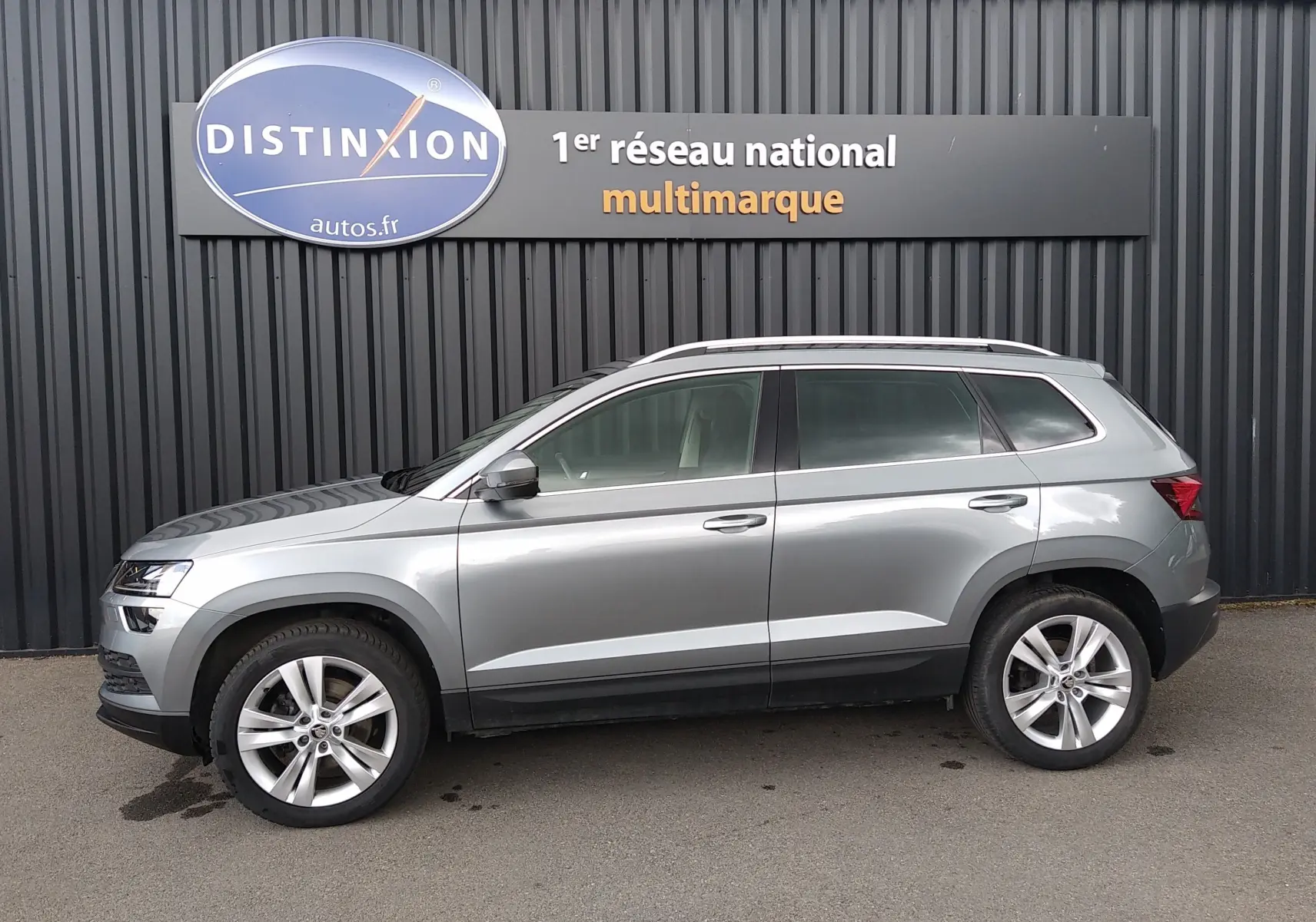 Vue latérale droite d'un Skoda Karoq gris 2022 avec jantes alliage et barres de toit chromées.