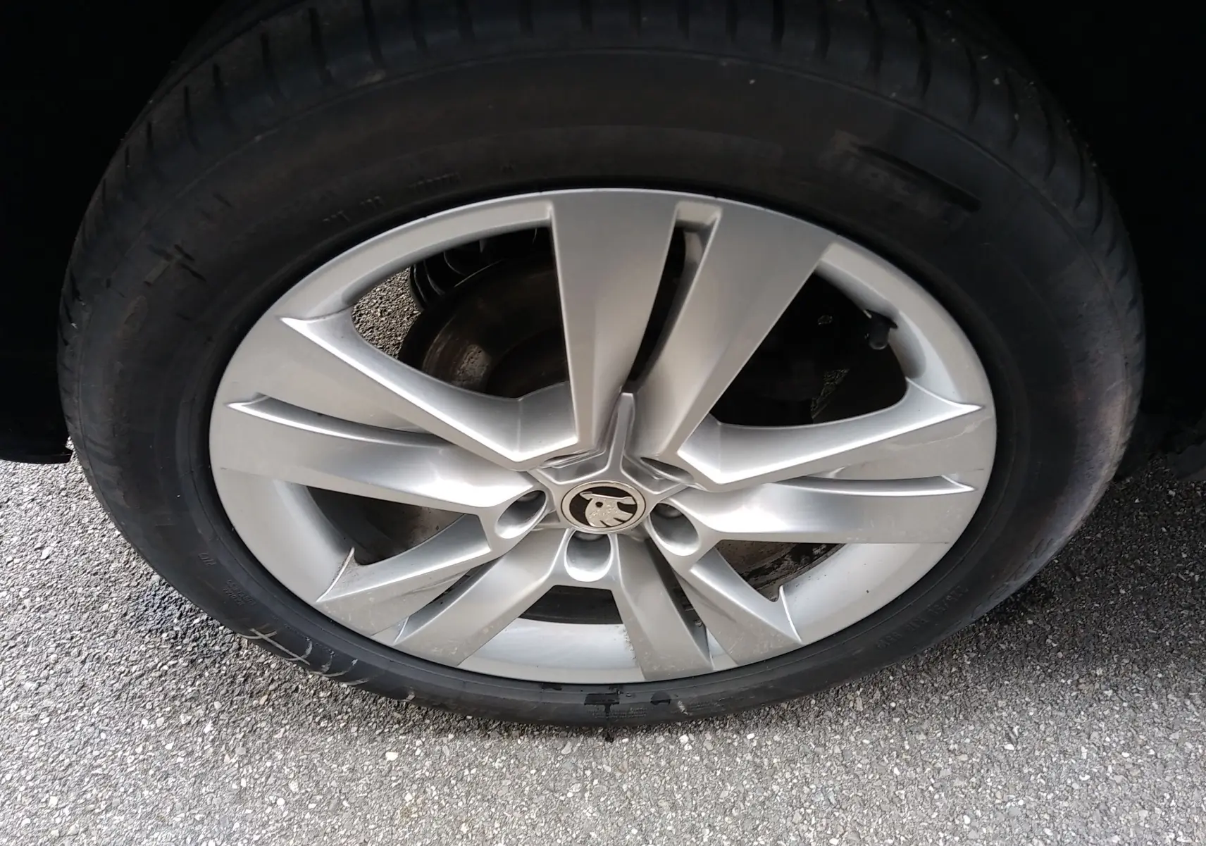 Gros plan sur la jante alliage argentée à 5 doubles branches du Skoda Karoq gris, avec logo central visible.