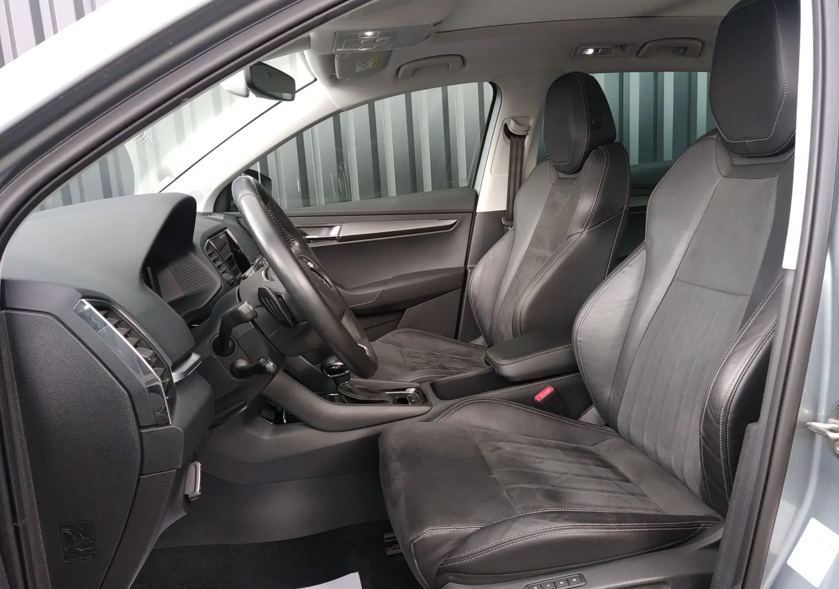 Vue intérieure côté conducteur du Skoda Karoq gris 2022, sièges en cuir et alcantara noirs avec coutures contrastées.