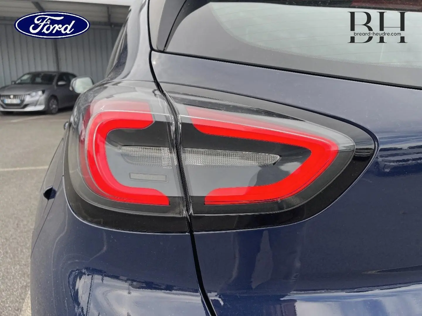 Gros plan sur le feu arrière gauche rouge et noir du Ford Puma bleu Abysse 2023, avec reflet du ciel et arrière-plan flou.