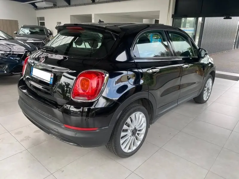 Vue 3/4 arrière droite d'une FIAT 500X noire brillante avec jantes alliage, stationnée en intérieur showroom.