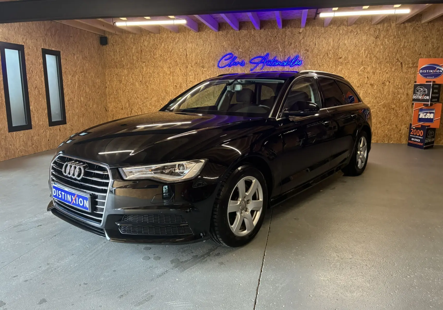Audi A6 Avant noire vue en 3/4 avant droit dans un showroom avec éclairage intérieur et mur en bois.
