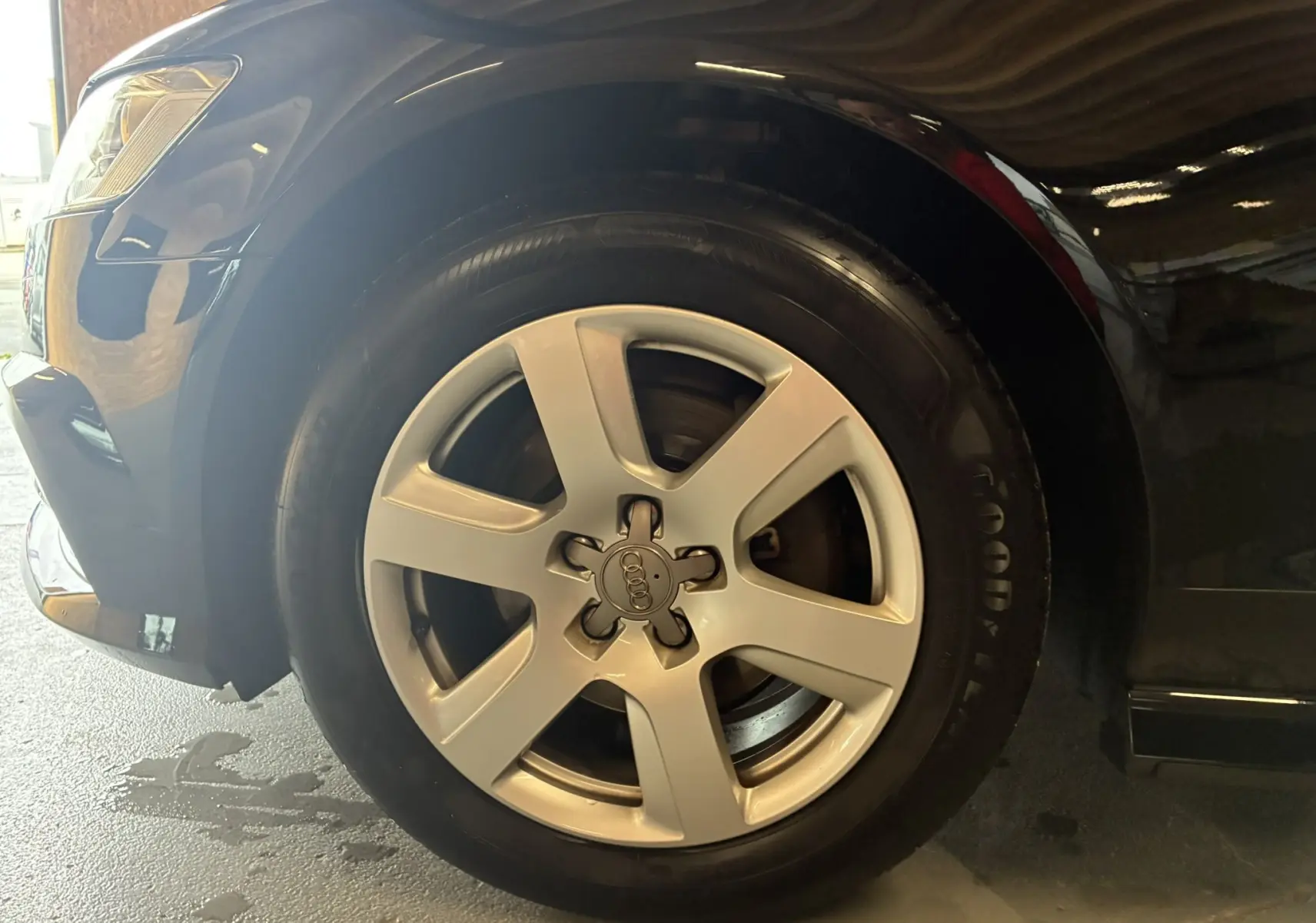 Gros plan sur la roue avant gauche d'une Audi A6 Avant noire de 2017 avec jante alliage cinq branches.