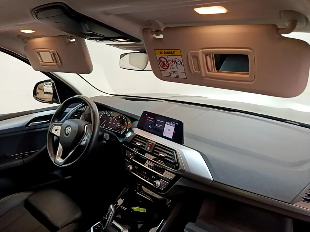 Vue intérieure côté conducteur du BMW X3 noir 2020, tableau de bord moderne avec écran tactile et volant multifonctions cuir.