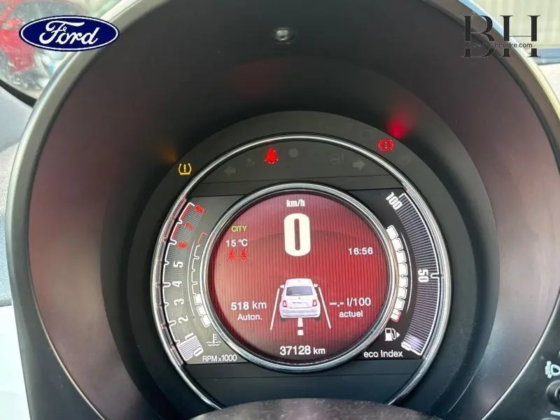 Vue rapprochée du tableau de bord numérique de la Fiat 500 blanche, affichant la vitesse à 0 km/h et diverses informations.