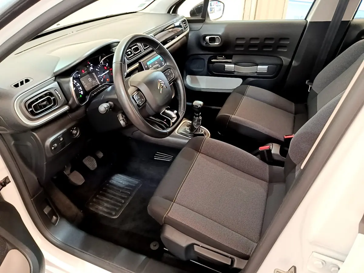 Intérieur avant droit de la Citroën C3 blanche 2019, volant cuir, tableau de bord moderne et sièges tissu gris.