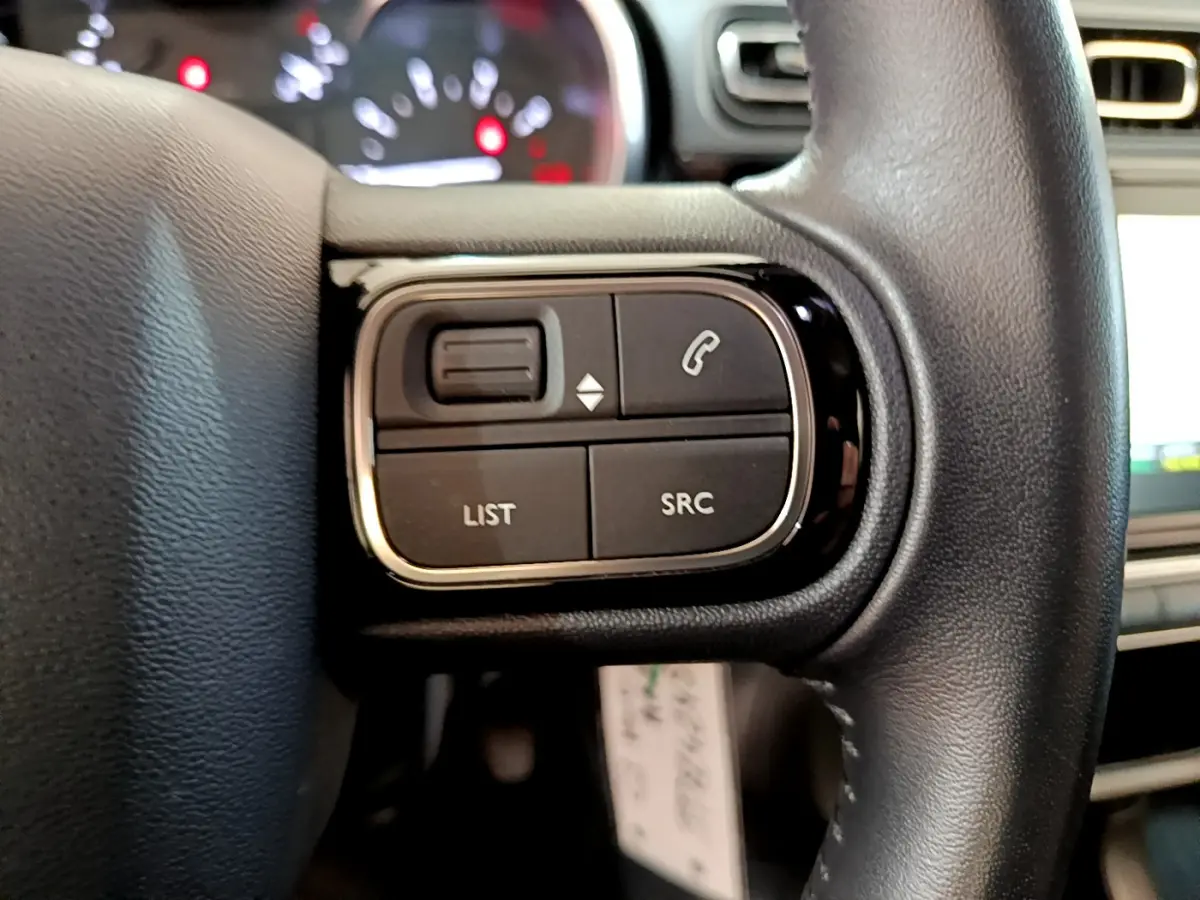 Gros plan sur les commandes gauche du volant cuir de la Citroën C3 blanche, avec boutons de téléphone et liste.