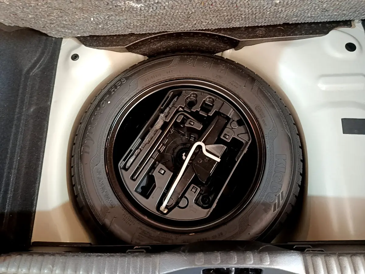 Roue de secours noire avec outils intégrés dans le coffre blanc d'une Citroën C3 blanche, vue de dessus.