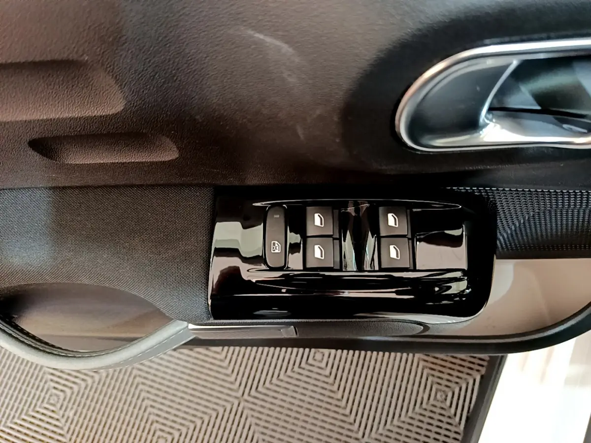 Commandes des vitres électriques sur la porte côté conducteur d'une Citroën C3 blanche, vue rapprochée intérieure.