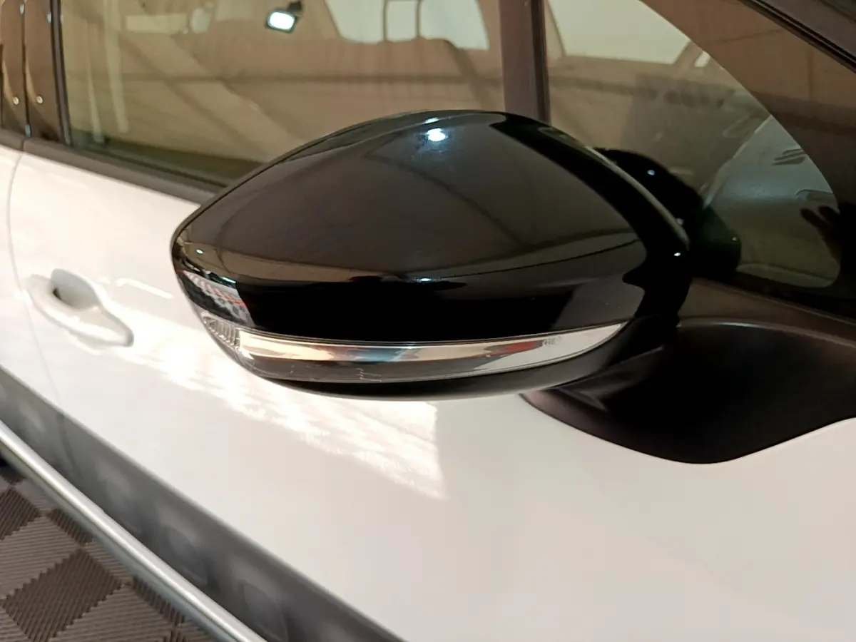 Rétroviseur noir brillant côté conducteur sur une Citroën C3 blanche vue de profil rapproché.