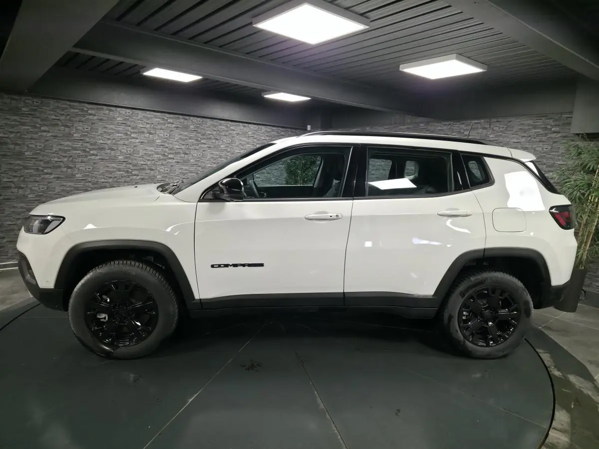 Jeep Compass blanc vu de profil côté gauche, avec jantes noires et détails noirs contrastants.