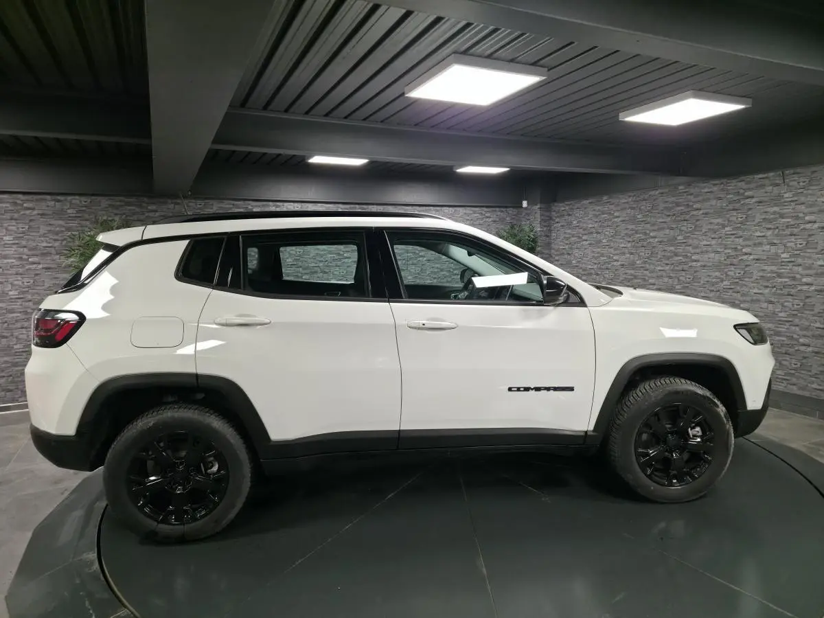 Profil côté gauche d'un Jeep Compass blanc avec jantes noires dans un garage moderne à lumière artificielle.