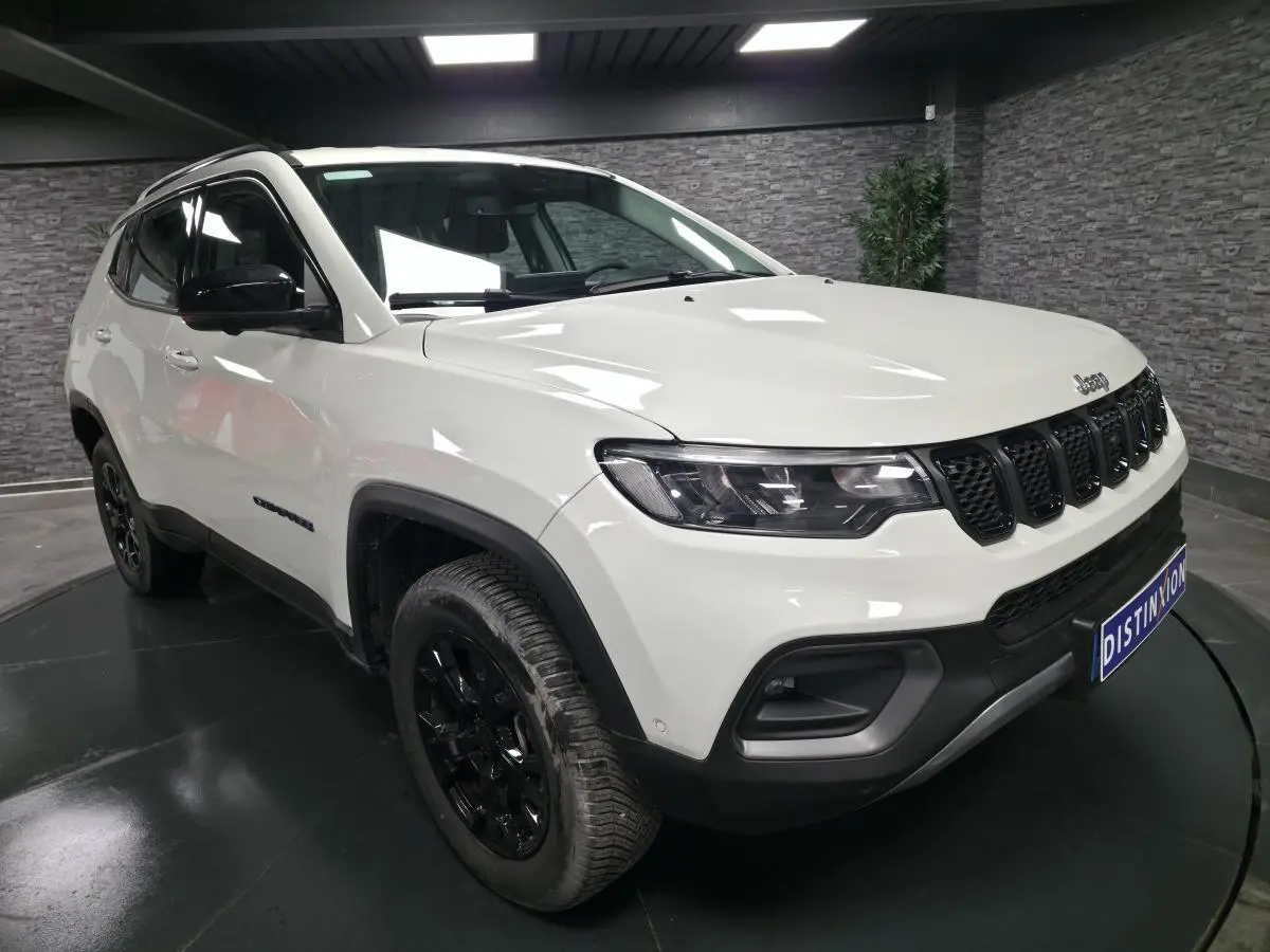 Jeep Compass blanc en 3/4 avant droit, avec jantes noires et calandre à sept fentes caractéristiques.