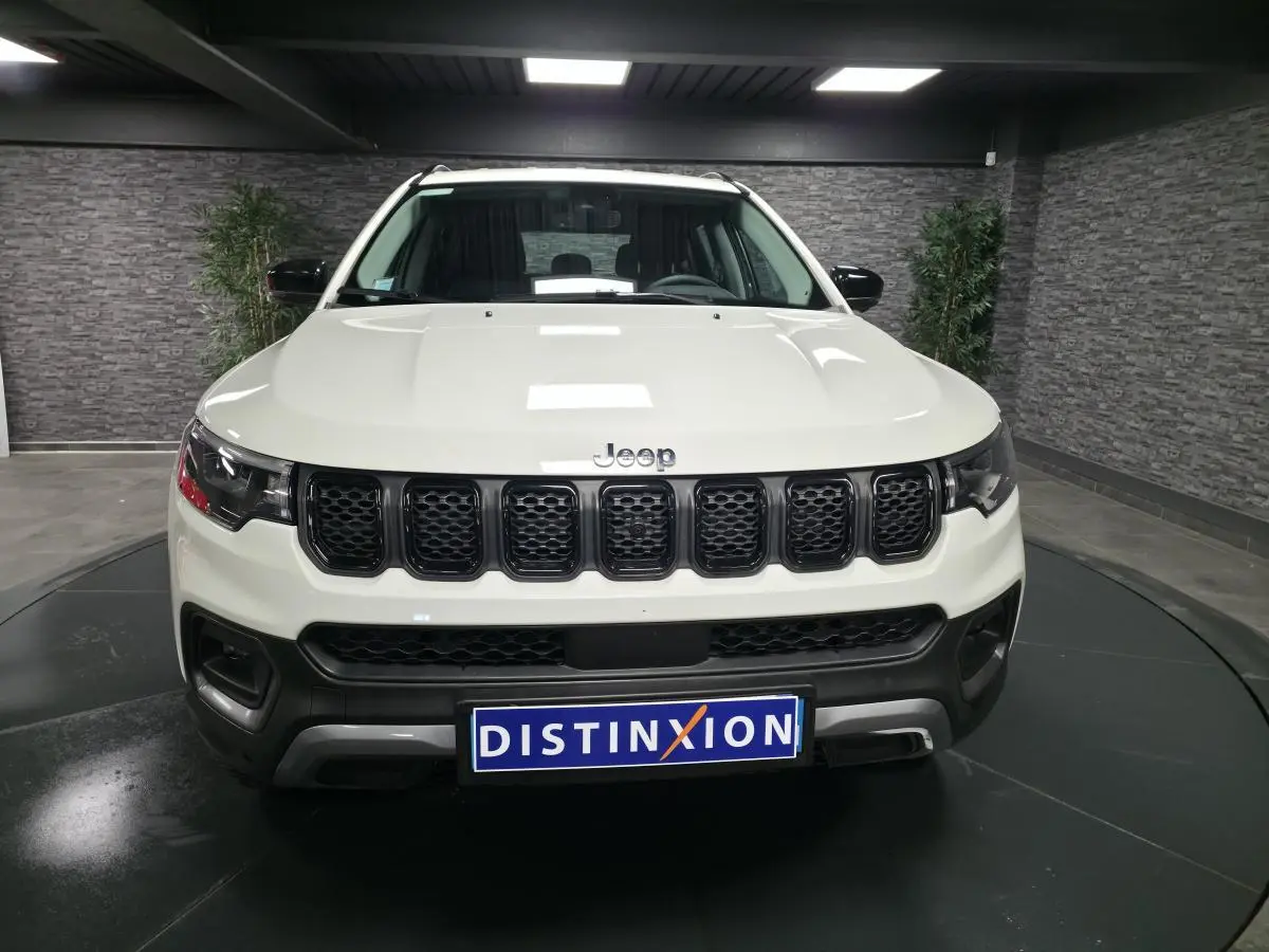 Vue frontale d'un Jeep Compass blanc avec calandre noire et plaque Distinxion en intérieur showroom.