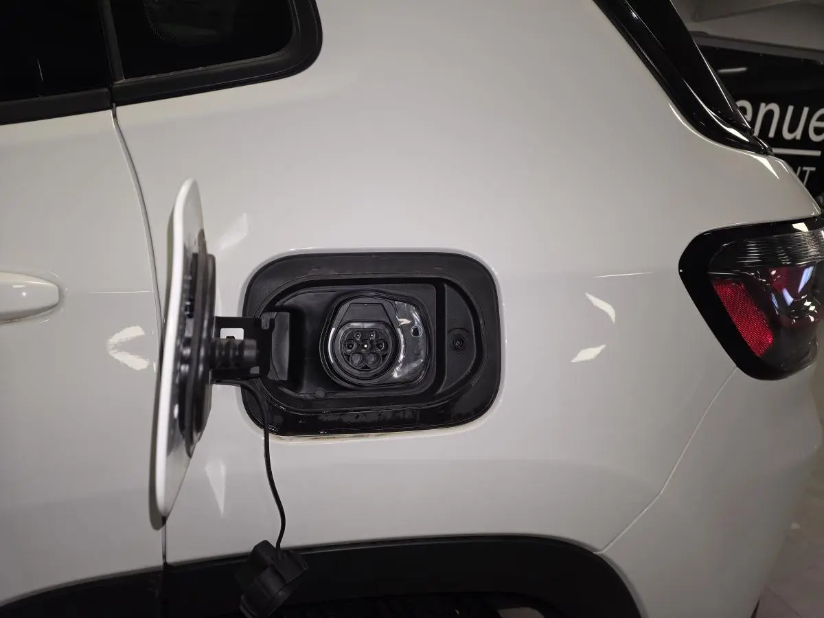 Prise de recharge ouverte côté gauche arrière d'un Jeep Compass blanc hybride rechargeable avec feu arrière visible.