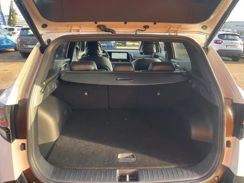 Vue arrière du coffre ouvert d'un KIA Sportage blanc nacré 2022, avec cache-bagages et intérieur noir visible.