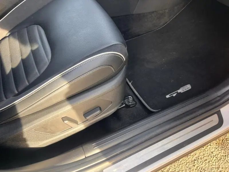 Vue rapprochée du siège conducteur noir en cuir synthétique avec commandes électriques et tapis de sol noir marqué GT-Line sur un Kia Sportage blanc.